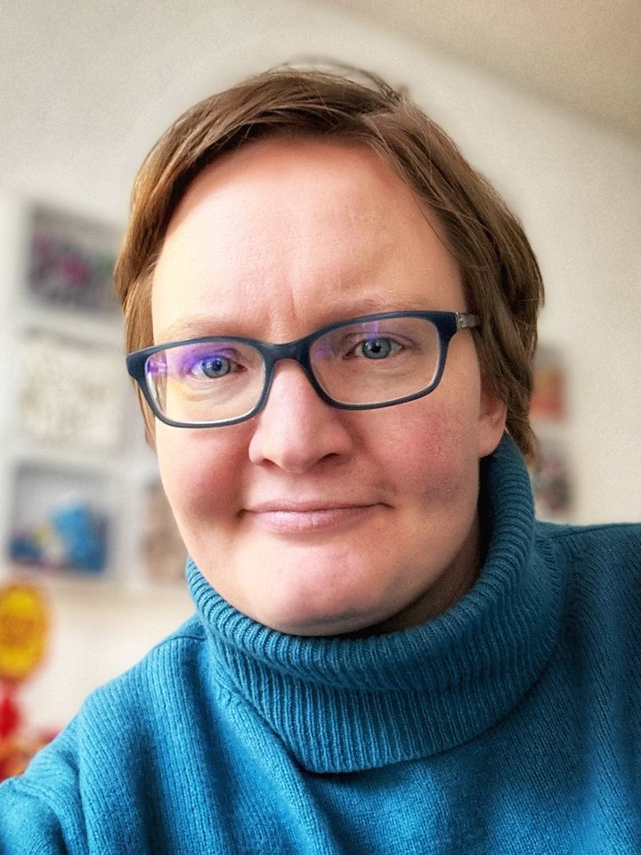 Porträt von Yvonne Pöppelbaum: kurze braune Haare, dunkle Brille, petrolfarbener Rollkragenpullover